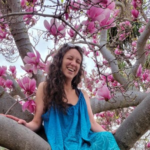 Könnte beinhalten: Eine Frau in einem blau-weiß gemusterten Kleid sitzt in einem Baum mit rosa Blüten. Das Kleid hat einen Rüschen-Saum und eine lockere, fließende Passform.