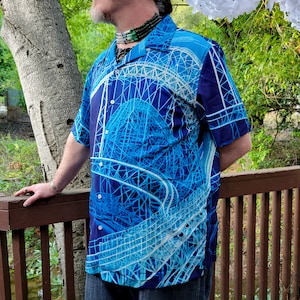 May include: A blue and white patterned short-sleeved shirt with a design of a roller coaster. The shirt has a button-down collar and a relaxed fit.