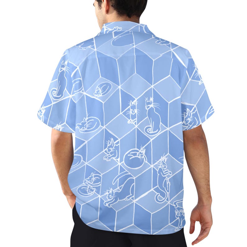 Puede incluir: Camisa azul claro de manga corta con un estampado repetido de ilustraciones de gatos blancos. Los gatos est&aacute;n en varias poses, sobre un dise&ntilde;o de cubos geom&eacute;tricos. La camisa tiene un cuello cl&aacute;sico.