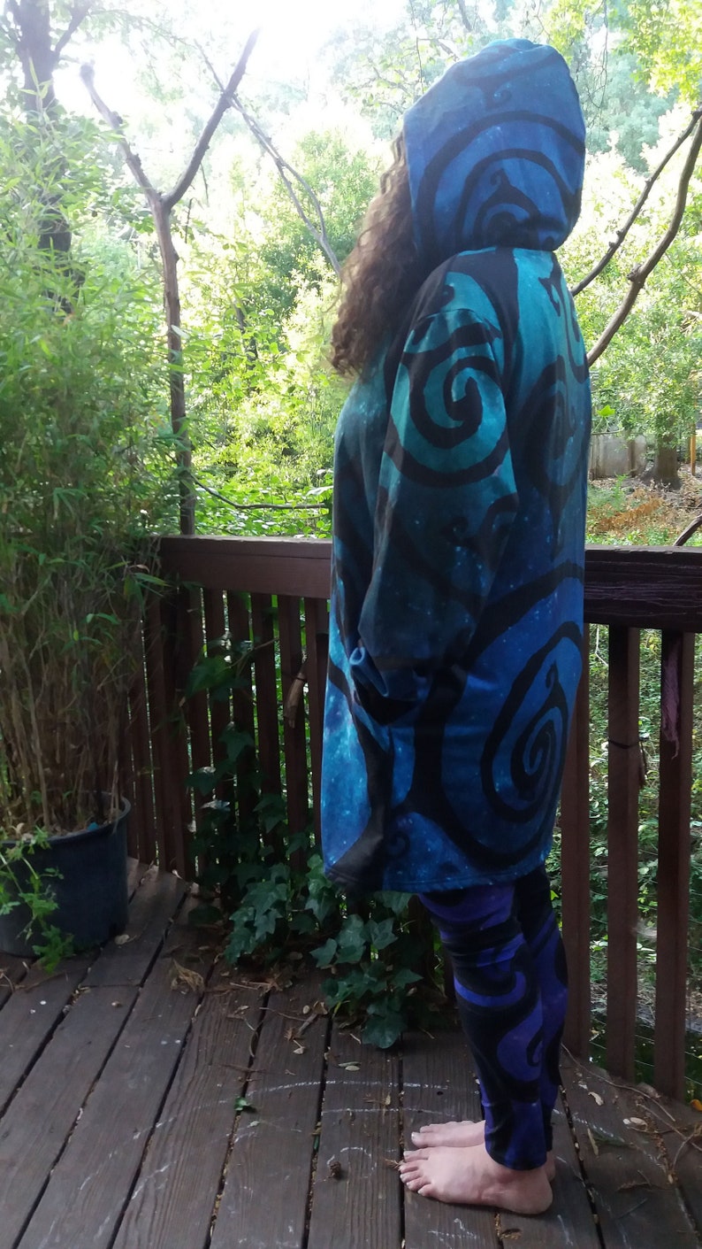 May include: A long-sleeved hooded sweatshirt with a blue and black swirling pattern. The sweatshirt is worn by a person standing on a wooden deck.