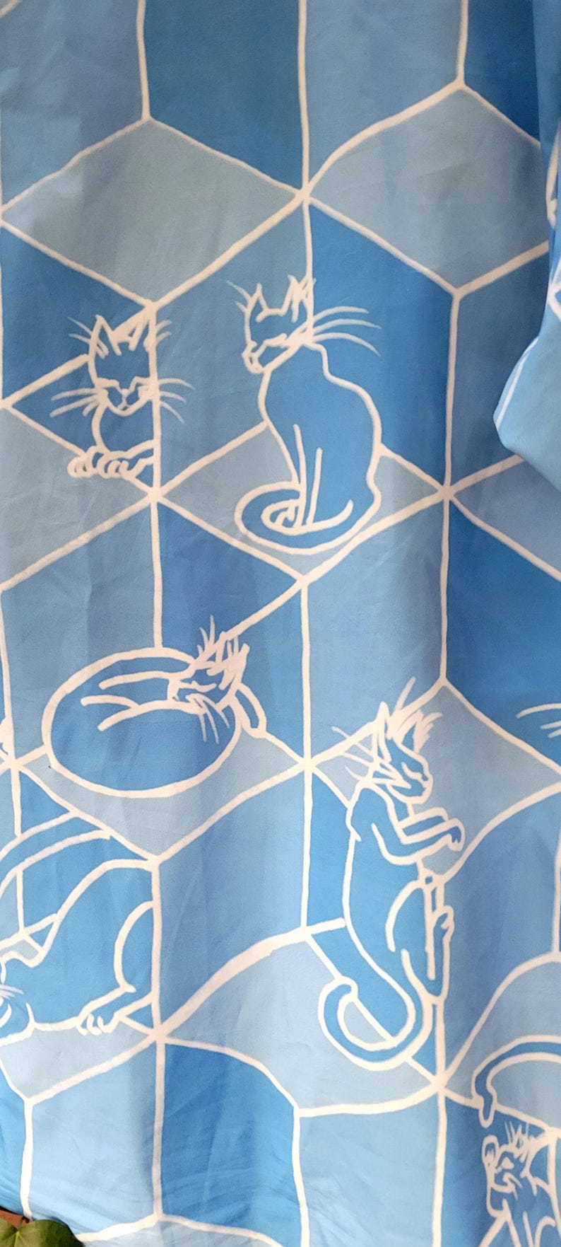 Puede incluir: Tela azul claro con un patr&oacute;n repetido de ilustraciones de gatos blancos dentro de un dise&ntilde;o geom&eacute;trico. Los gatos se representan en varias poses, incluyendo sentados, acurrucados y de pie.