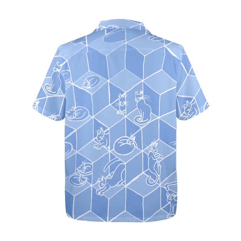Puede incluir: Camisa azul claro de manga corta con un estampado repetido de ilustraciones de gatos blancos. Los gatos est&aacute;n en varias poses, sobre un dise&ntilde;o de cubos geom&eacute;tricos. La camisa tiene un cuello cl&aacute;sico.