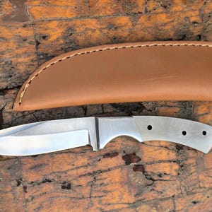 May include: A silver knife with a brown leather sheath. The knife has a plain blade and a handle with four holes.