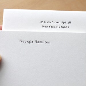 May include: A white envelope with a white card inside. The envelope has the address 55 E 4th Street, Apt. 3H, New York, NY 10003 printed on it. The card has the name Georgia Hamilton printed on it.