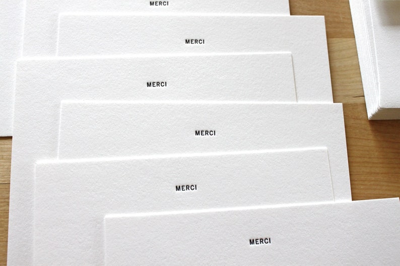 May include: Stack of white cards with the word "MERCI" printed on each card.
