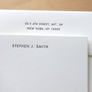 May include: A white envelope with a white card inside. The envelope has the address 55 E 4TH STREET, APT. 3H NEW YORK, NY 10003 printed on the front. The card has the name STEPHEN J. SMITH printed on the front.