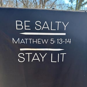 以下が含まれることがあります： 黒と白のサインに「BE SALTY」と「MATTHEW 5:13-14」の文字が書かれており、その下に線が引かれ、「STAY LIT」の文字が書かれている。