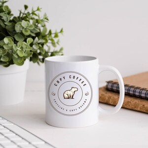 May include: White ceramic mug with a brown logo that says "Capy Coffee" and features a cartoon capybara. The logo also includes the text "Caffeine & Capy Dreams".