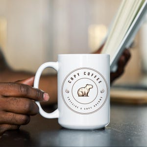 May include: White ceramic coffee mug with a brown graphic of a capybara and the text "Capy Coffee Caffeine & Capy Dreams".