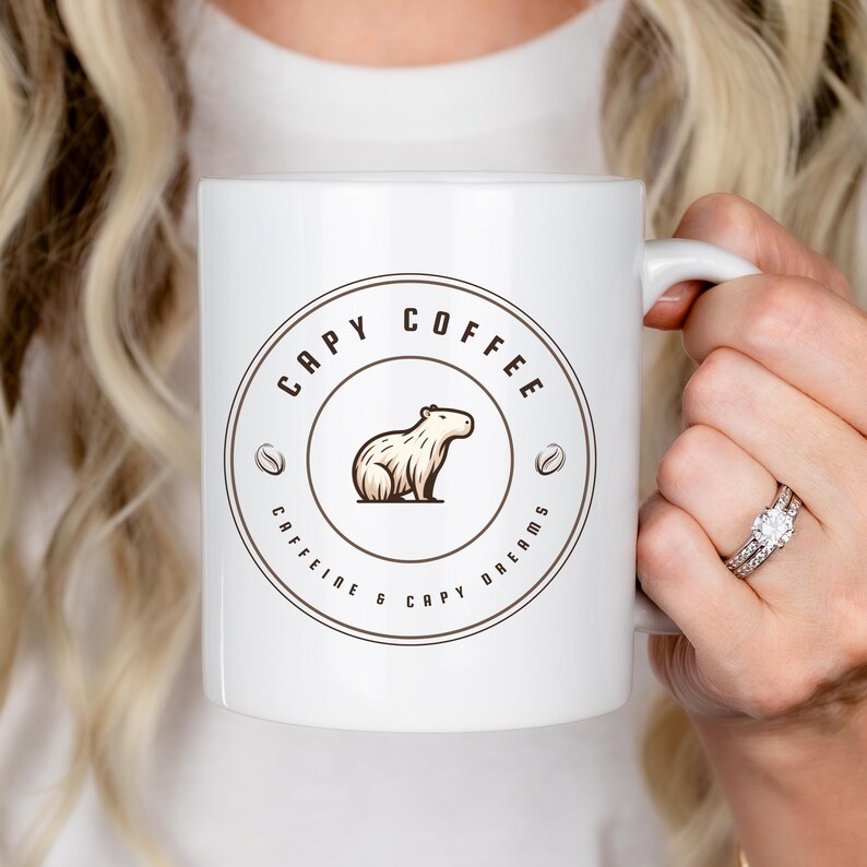 May include: White ceramic mug with a brown circle design featuring a cartoon capybara and the text "Capy Coffee Caffeine & Capy Dreams".