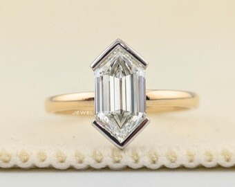 May include: A ring featuring a clear, elongated hexagonal-cut gemstone set in a silver-toned bezel. The band is crafted from a smooth, polished yellow gold metal. The text JEWEL NESTS is visible in small, faint lettering on the gemstone surface.