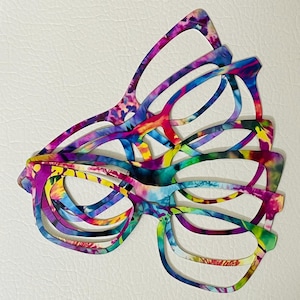 Puede incluir: Una pila de gafas coloridas con estampado tie-dye. Las gafas son de varios tonos de rosa, morado, azul, verde y amarillo.