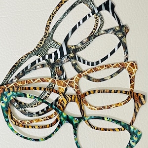 May include: A stack of five pairs of eyeglasses with different animal print patterns, including leopard, zebra, giraffe, tiger, and peacock. The glasses are all black and have a modern, stylish design.