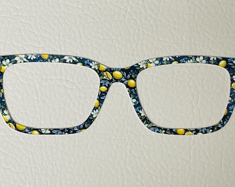 May include: A pair of square-shaped glasses with a floral print featuring yellow lemons and white flowers on a dark blue background.
