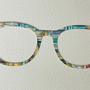 以下が含まれることがあります： カラフルな本のプリントデザインが施された眼鏡。眼鏡は硬質プラスチック製で、丸みを帯びた形をしています。