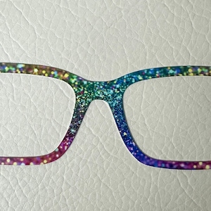 Puede incluir: Un par de gafas de purpurina arcoíris con montura cuadrada.
