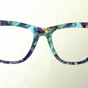 Könnte beinhalten: Eine Brille mit einem abstrakten Muster in Teal, Lila und Gold.