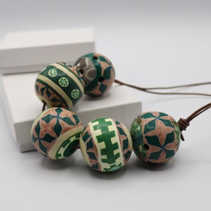 May include: A necklace with six green and brown patterned beads. The beads are round and have a geometric design. The necklace is made of brown cord.