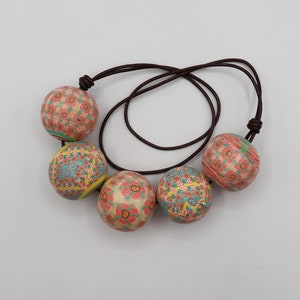 May include: A necklace made of brown cord with five colorful round beads. The beads are decorated with a floral pattern in shades of pink, blue, and yellow.