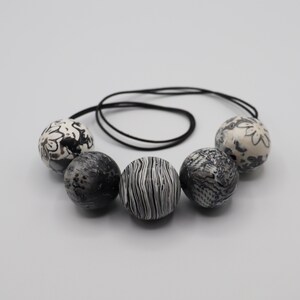 May include: A black and white necklace with five large round beads. The beads have different patterns, including floral, striped, and textured.