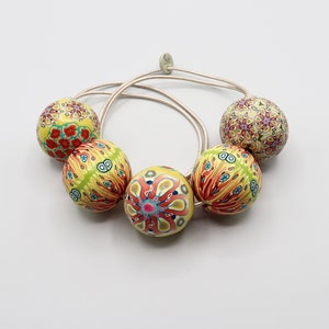 May include: A silver necklace with five yellow, red, and green patterned beads. The beads are round and have a floral design.