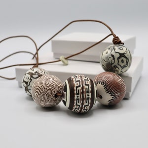 May include: A brown leather cord necklace with five large, round, white and brown patterned beads. The beads have different geometric and floral designs.