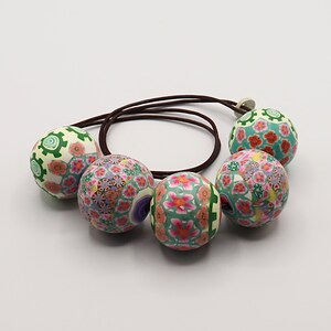 May include: A necklace with five large, round beads. The beads are made of polymer clay and have a colorful floral pattern in shades of green, pink, and white. The necklace is strung on a brown cord.