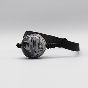 May include: A black leather bracelet with a white and black patterned bead.