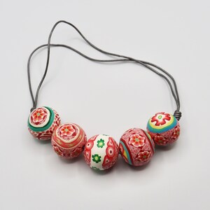 May include: A necklace with a gray cord and five large, round, colorful beads. The beads are decorated with intricate floral patterns in shades of red, white, green, and blue.