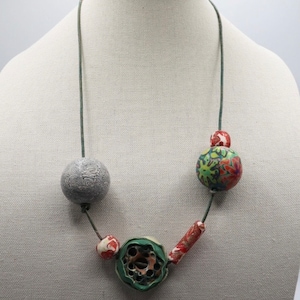 May include: A green, gray, and red polymer clay necklace with a variety of patterned beads. The necklace is on a green cord.