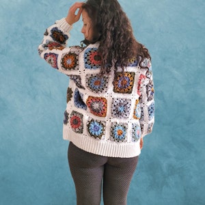 Peut inclure: Un cardigan blanc en crochet avec des carrés de grand-mère colorés. Le cardigan a une coupe ample et des manches longues.