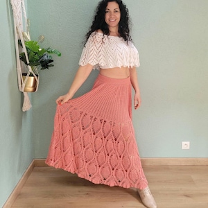 Peut inclure: Une jupe longue en crochet corail avec un motif délicat de feuilles. La jupe est fluide et a une taille haute.