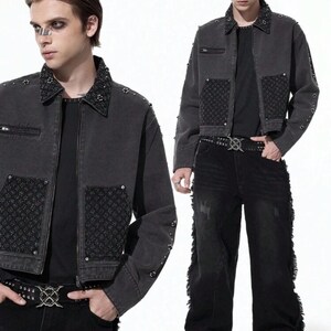 May include: A dark gray denim jacket with studded accents on the collar and sleeves. The jacket features a zip pocket and decorative patches. The model is wearing black jeans and a studded belt, creating a gothic or punk aesthetic.