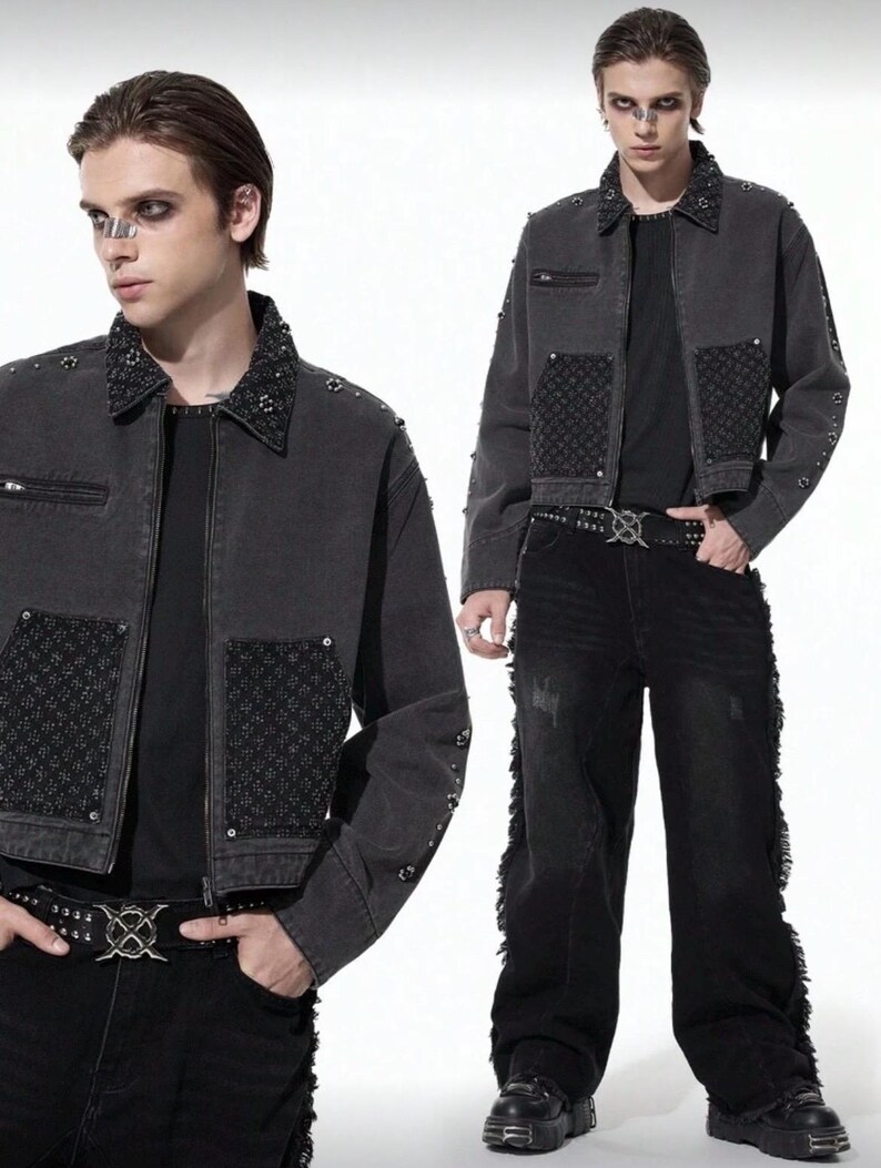 May include: A dark gray denim jacket with studded accents on the collar and sleeves. The jacket features a zip pocket and decorative patches. The model is wearing black jeans and a studded belt, creating a gothic or punk aesthetic.