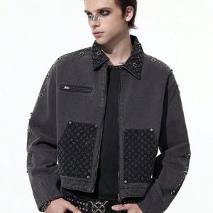 May include: A dark gray denim jacket with a studded collar and pocket details. The jacket features a zipper closure and decorative studs on the sleeves. A black belt with a silver buckle is also visible.