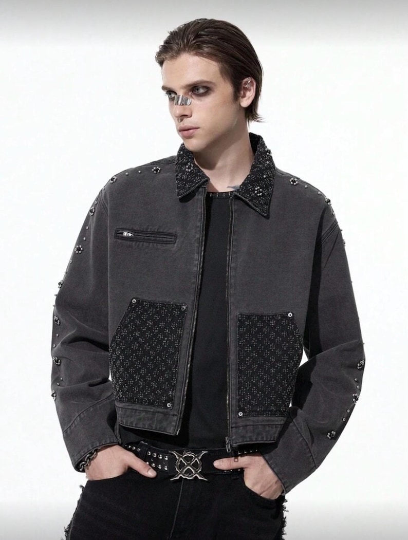 May include: A dark gray denim jacket with a studded collar and pocket details. The jacket features a zipper closure and decorative studs on the sleeves. A black belt with a silver buckle is also visible.