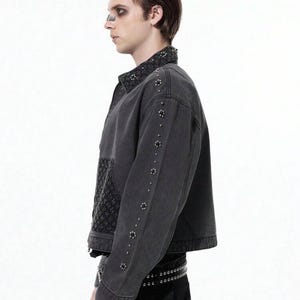 May include: A dark gray denim jacket with decorative studs along the sleeves and collar. The jacket features a textured panel on the front and a studded belt. The jacket is a stylish piece of outerwear.