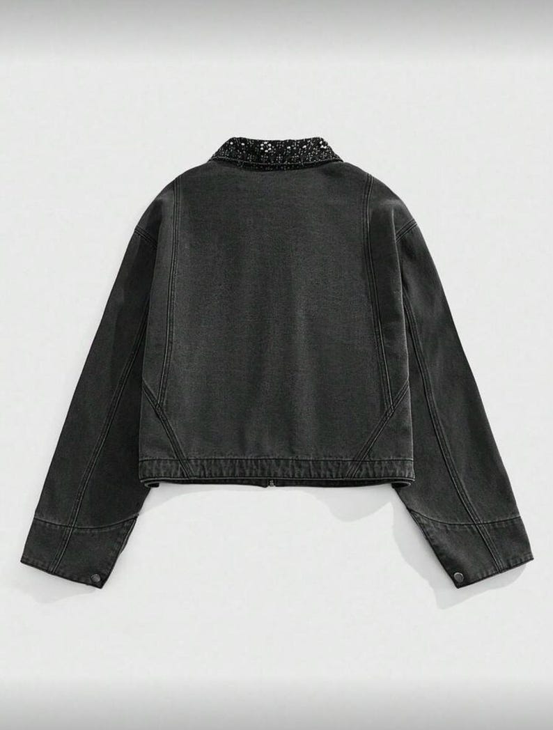 May include: A dark gray denim jacket with a decorative collar. The jacket has long sleeves, a button closure on the cuffs, and a zipper closure down the front. The back of the jacket is visible, showing the seams and construction details.