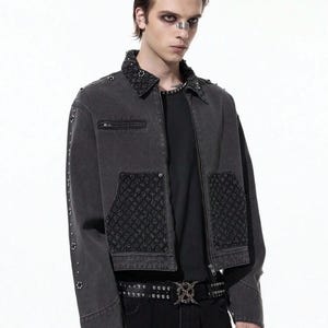 May include: A dark gray denim jacket with a studded collar, pocket accents, and sleeve details. The jacket features a zipper closure and is paired with a black belt with a decorative buckle. The jacket is part of a fashion ensemble.