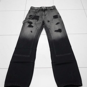 Può includere: Jeans in denim neri e grigi con un design sbiadito e strappato. Presentano una cintura, una catena e decorazioni a forma di croce sulle tasche e sulla parte inferiore delle gambe. I jeans hanno un taglio a gamba larga.