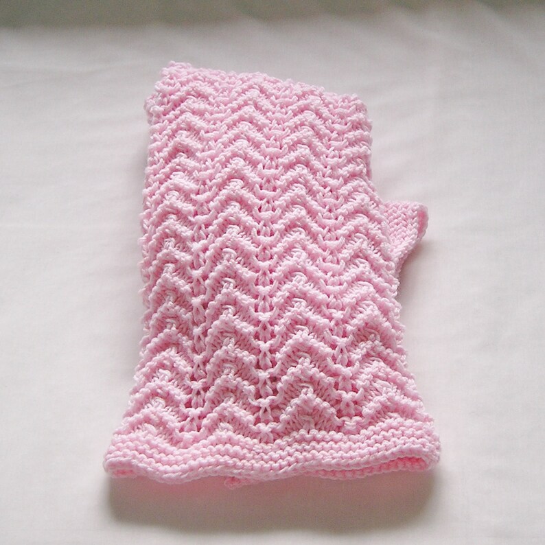 May include: A light pink knitted fingerless glove with a chevron pattern. The glove is made of soft yarn and has a ribbed cuff. The open finger design allows for dexterity while keeping the hand warm.