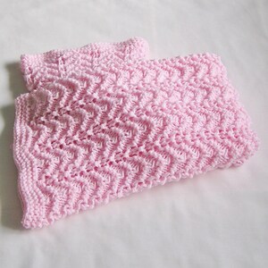 May include: A pair of light pink knitted baby blankets. The blankets feature a textured, zig-zag pattern. The soft, pastel color and intricate knit design suggest a handmade or artisanal quality, suitable for a nursery or as a baby gift.
