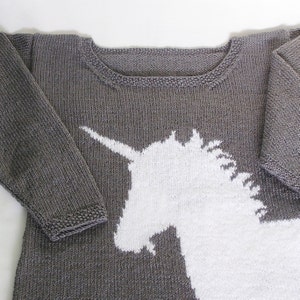 May include: A gray knitted sweater with a white unicorn design. The sweater has long sleeves and a crew neck.