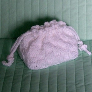 May include: A white crocheted drawstring bag with a gathered top. The bag is made with a textured stitch and has a soft, fluffy appearance.