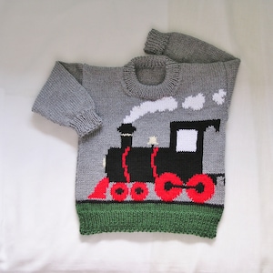 May include: A gray knitted sweater with a black and red train design. The train has a white smoke plume and is on a green field.