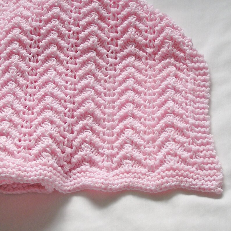 May include: A close-up of a soft pink knitted hat. The hat features a chevron pattern throughout the body and a ribbed edge. The hat is made of a soft, textured yarn, perfect for a baby.