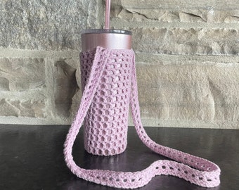 May include: A pink crocheted tumbler holder with a long strap. The holder is designed to fit a standard size tumbler and has a delicate, open-weave pattern.
