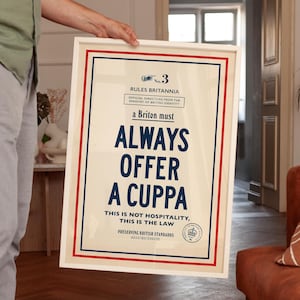 May include: A framed poster with a cream background, red and blue borders, and text that reads: No. 3 RULES BRITANNIA OFFICIAL DIRECTIVES FROM THE MINISTRY OF BRITISH IDENTITY a Briton must ALWAYS OFFER A CUPPA THIS IS NOT HOSPITALITY, THIS IS THE LAW.