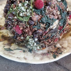 May include: A round, brown, and green decorative object covered in dried flowers, leaves, and berries. The object is sitting on a white plate.