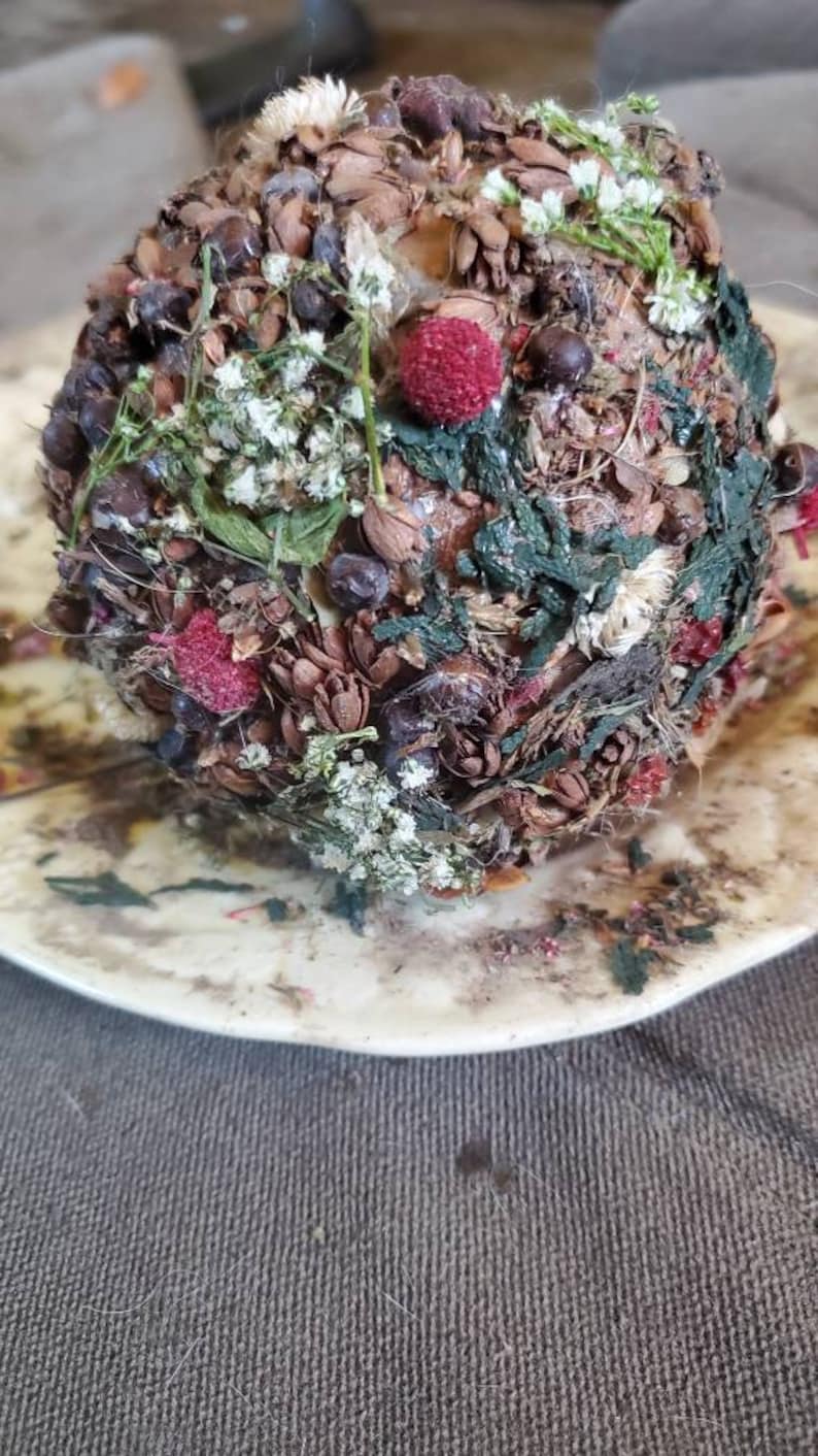 May include: A round, brown, and green decorative object covered in dried flowers, leaves, and berries. The object is sitting on a white plate.